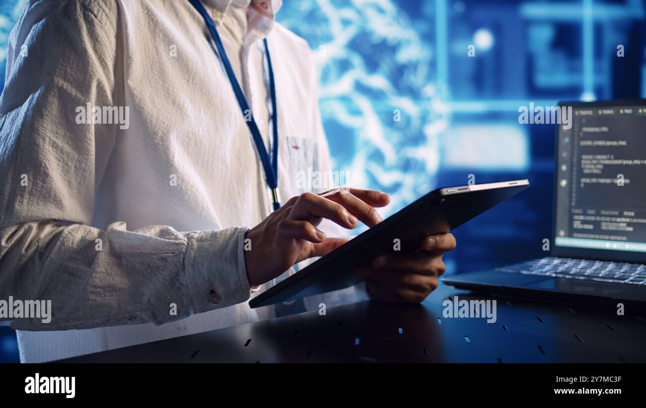 Computer scientist in data center, solving tasks on tablet while running programming scripts on laptop terminal. Certified engineer manipulating lines of code for AI applications development Stock Photo