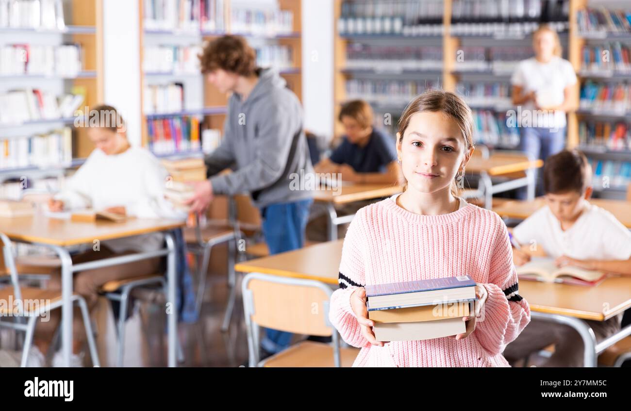 Girl with pile of books in library Stock Photo - Alamy