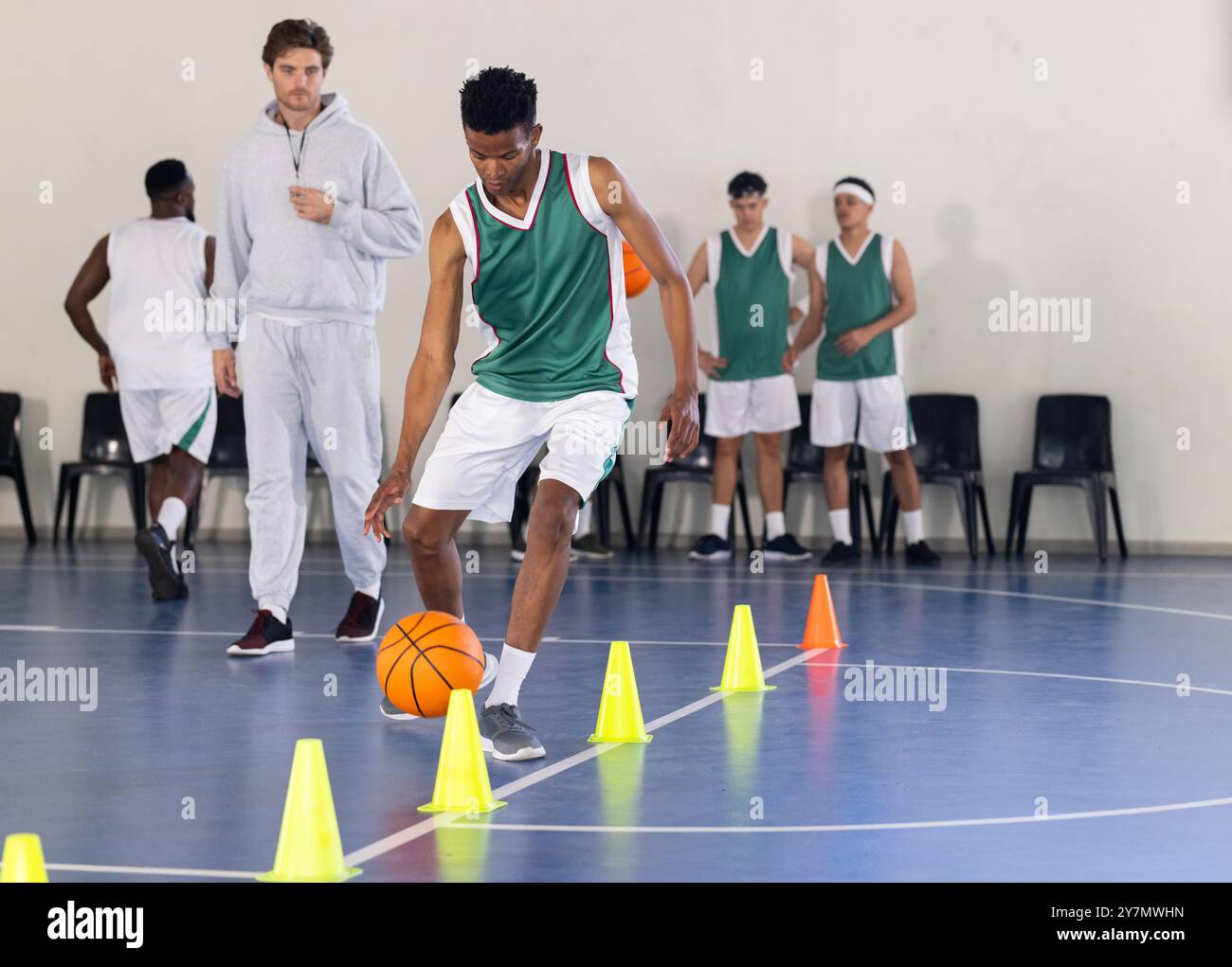 Dribbling basketball through cones, student practicing skills in school gym Stock Photo