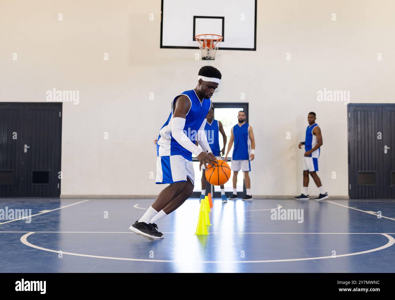 Dribbling basketball around cones, athlete practicing skills on indoor court Stock Photo