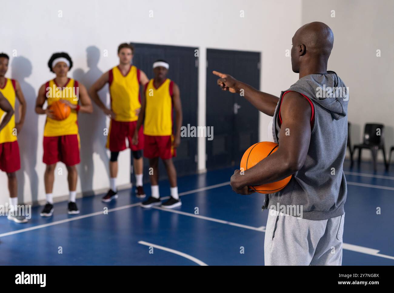 Coach holding basketball and instructing team of players during practice session Stock Photo