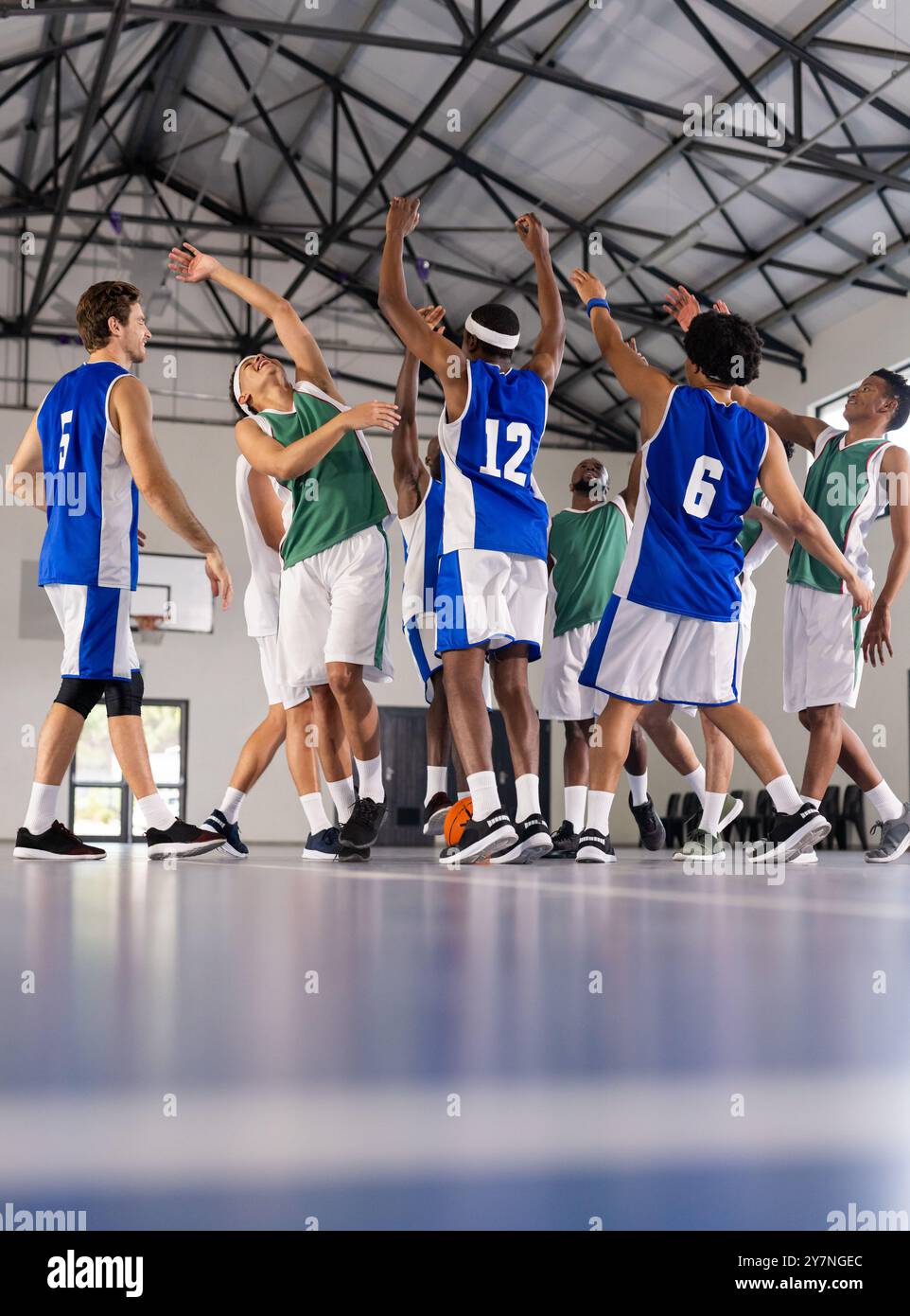 Playing basketball, team members in blue and green jerseys competing indoors Stock Photo