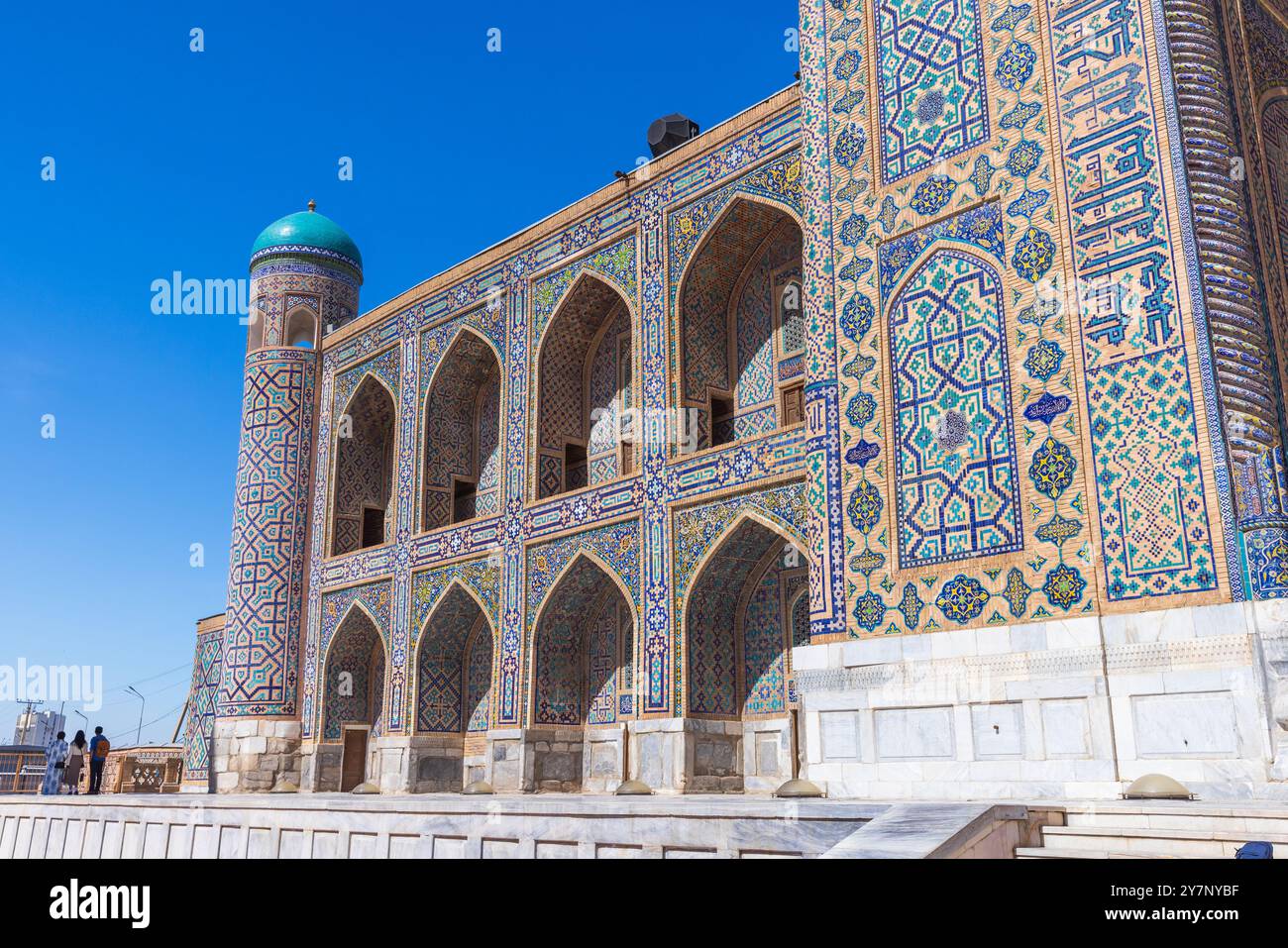 Samarkand, Uzbekistan - March 25, 2024: Tilya-Kori Madrasah facade on a sunny day. Tourists walk the Registan square Stock Photo