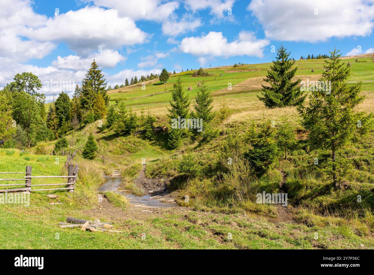 rural landscape in mountains. sunny autumn day. carpathian countryside of ukraine. scenery with haystacks and wooden fence. fluffy clouds on the sky Stock Photo