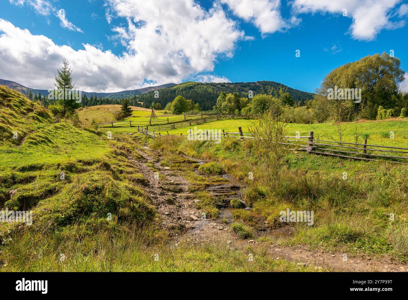 rural landscape in mountains. sunny autumn day. carpathian countryside of ukraine. scenery with haystacks and wooden fence. fluffy clouds on the sky Stock Photo