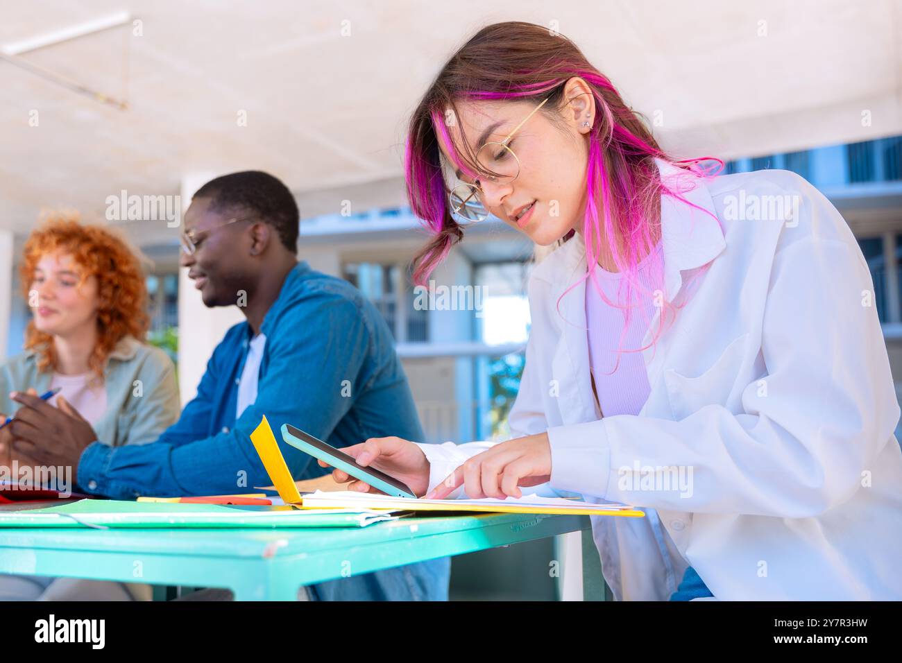 Three happy multiracial students studying with smartphones outdoors. Stock Photo