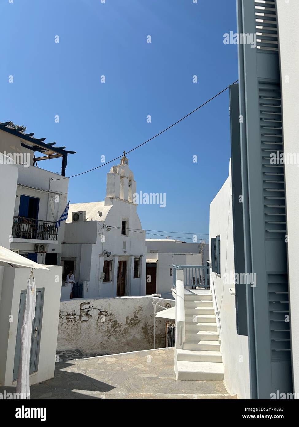 Greek island path picturing a white church in the sunlight among residential houses - Smartphone Captured Stock Image