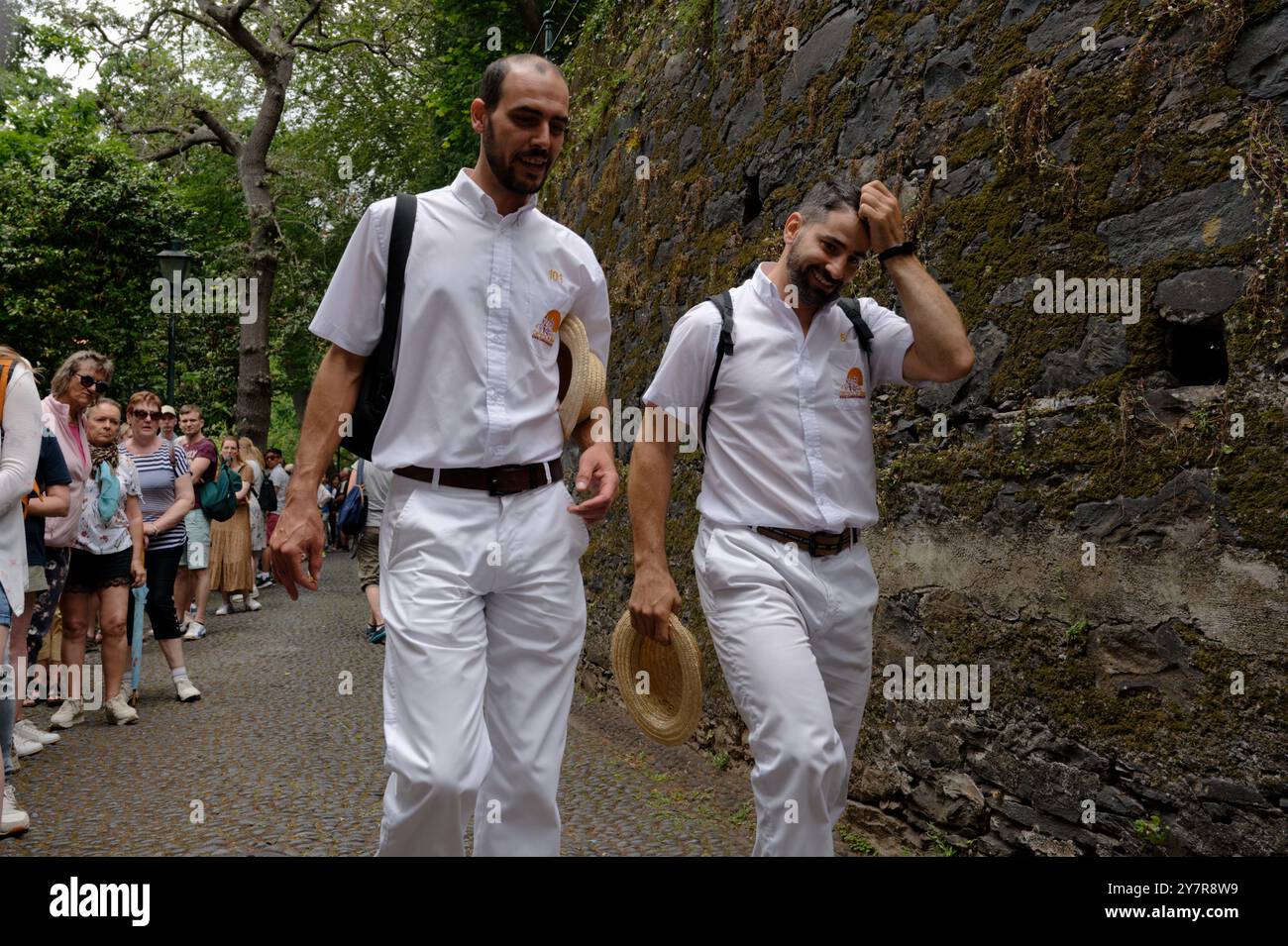 Two carreiros share a light moment, hats in hand, as they walk toward their next monte sled ride Stock Photo