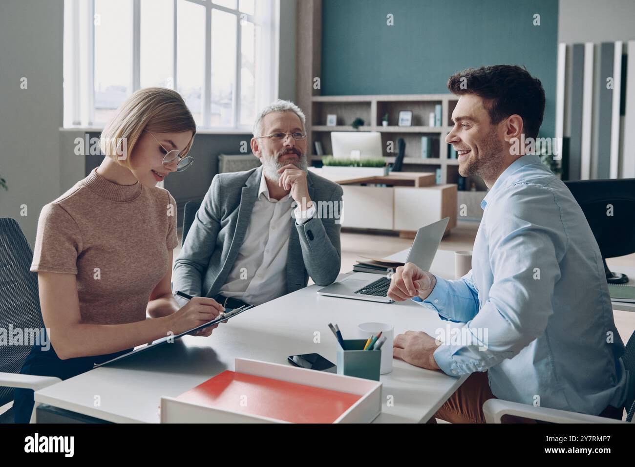 Happy young man having interview with HR managers while sitting at the office desk Stock Photo