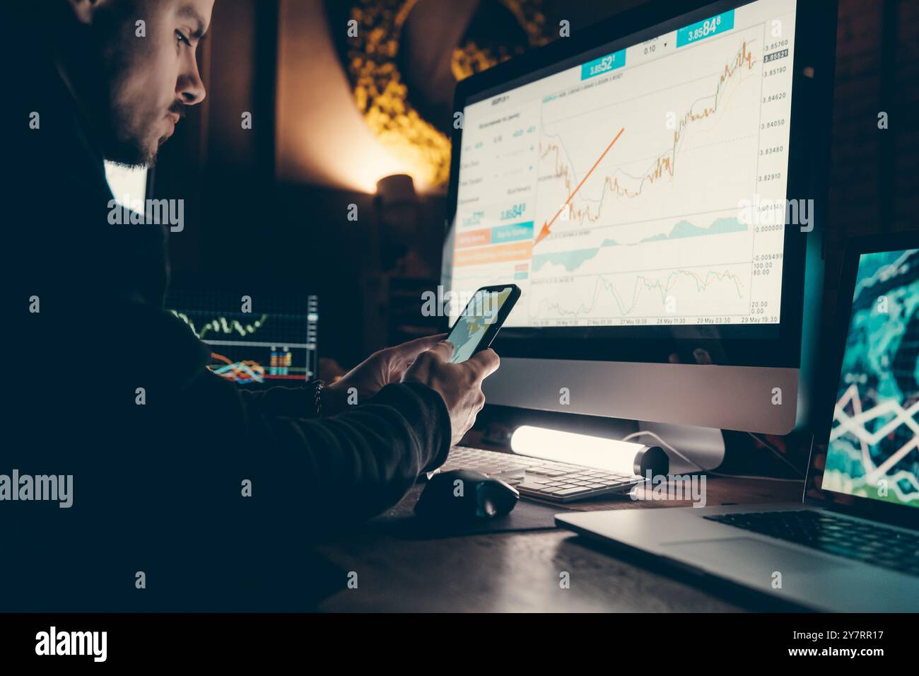 Close-up of confident young male stock trader using smart phone and computers while working late in office Stock Photo