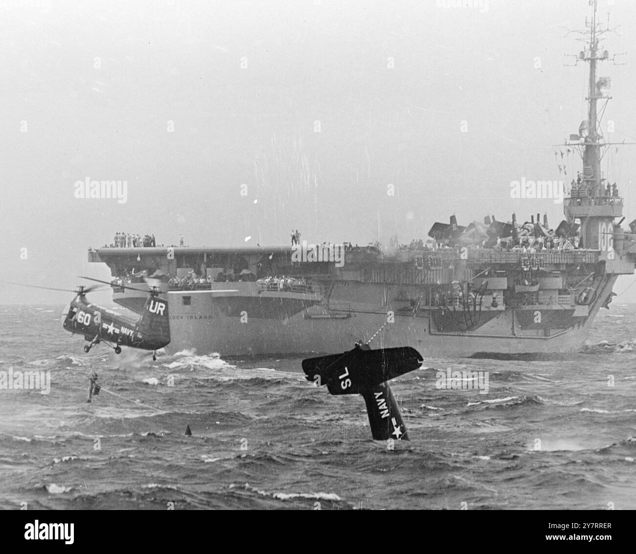 PARACHUTE WHICH NEARLY COST A LIFE 14.8.53. A parachute, often the means of saving a flyer's life, nearly cost Ensign E. H. Barry, a U.S. Navy airman, his. When his Grumman fighter plunged into the sea, after taking off from a carrier, Barry's parachute opened and waged a tug-of-war with the helicopter which was trying to pull him from the sea. Eventually the rescue attempt was successful. I.N.P. photo shows As his aircraft sinks nose-first, Barry ( withings) is being hauled from the water by the helicopter. First of two-picture series 1/PJ/70578 International News Photos Stock Photo