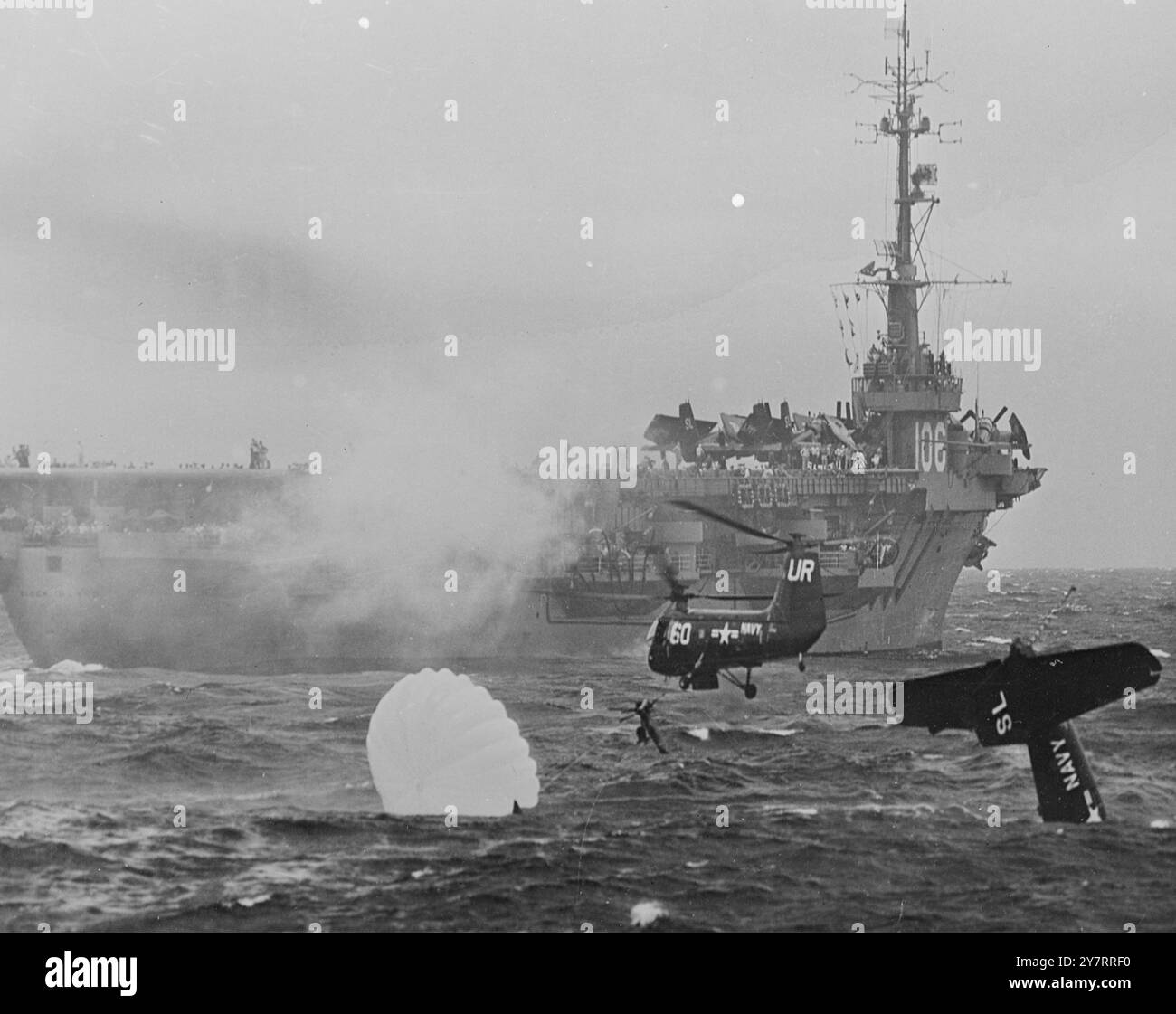 PARACHUTE WHICH NEARLY COST A LIFE 14.8.53. A parachute, often the means of saving a flyer's life, nearly cost Ensign E. H. Barry, a U.S. Navy airman, his. When his Grumman fighter plunged into the sea after taking off from a carrier, Barry's parachute opened and waged a tug-of-war with the helicopter which was trying to pull him from the sea. Eventually, the rescue attempt was successful. I.N.P. photo shows Barry (arrowed) hanging from the helicopter sling but his opened parachute, held by the water, is pulling against him. Second of two-picture series - International News Photos Stock Photo