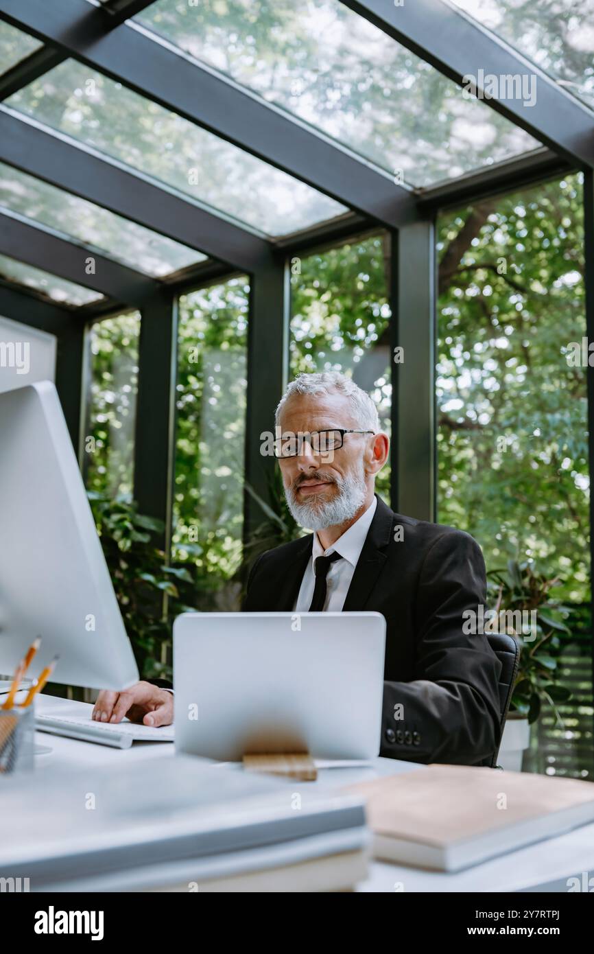 Serious mature businessman using computer while working in the modern ...