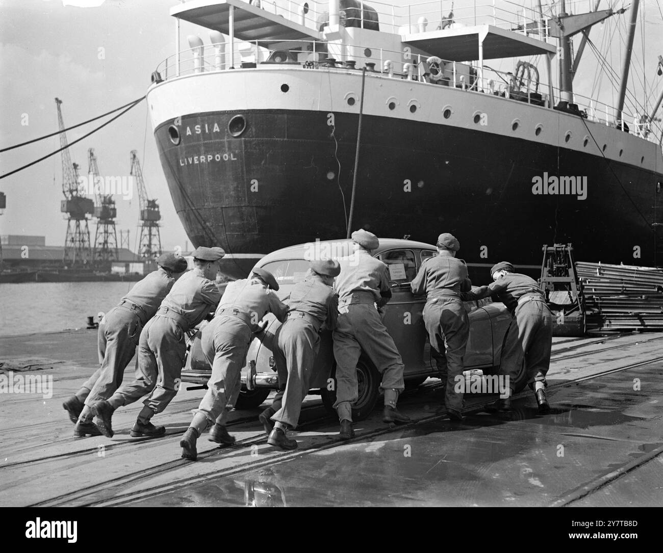 BIG PUSH BY TROOPS IN THE EXPORT DRIVE 25 April 1950  Another 1420 servicemen were drafted to the London Docks today (Tuesday) to join the 1000 who began moving cargoes yesterday.  Over 12400 dock workers are now out on strike, and only 26 of the 111 ships in port worked normally yesterday.  Picture Shows: Servicemen pushing one of the cars for export to Canada, at the King George V Dock, London  today.  In the background is the Asia on which cars will be loaded. Stock Photo