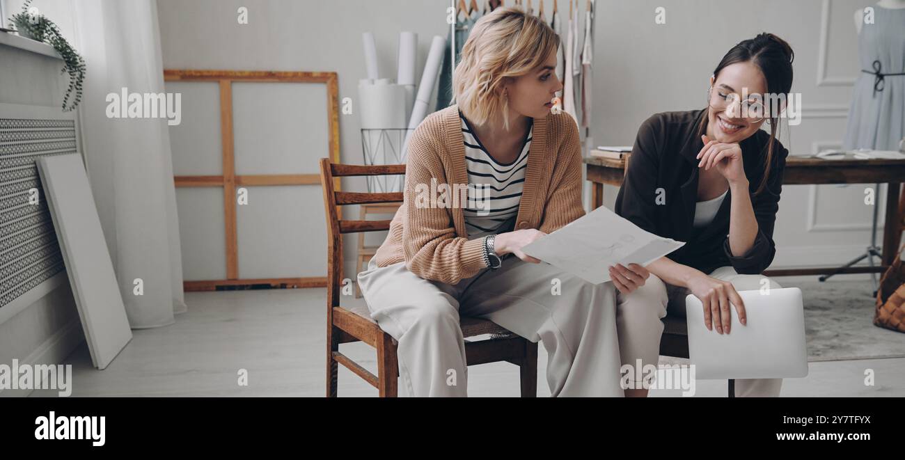 Two female fashion designers discussing new project while working in workshop Stock Photo