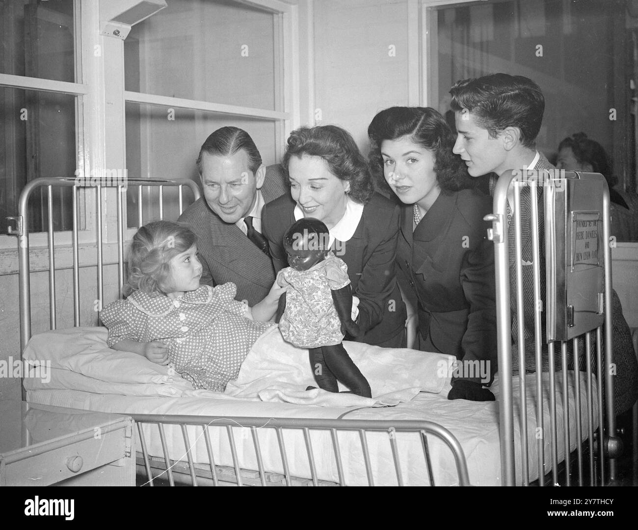 A SMALL PATIENT GETS A PRESENT FROM BEBE AND BEN  On the first official outing since her recent attack of food poisoning, Bebe Daniels, with her husband Ben Lyon, stars of the B.B.C. programme ' High! Gang ', visited the Queen Elizabeth Hospital for children ,  Banstead, Surrey, today to brighten the day for a small patient with the gift of a doll . While at the hospital, the radio, stage and film entertainers saw for the first time the two cots endowed by their joint ' fan clubs'.  PICTURE SHOWS:- A little shy, three-year-old Carol Meyers of East London received a gift from her distinguished Stock Photo