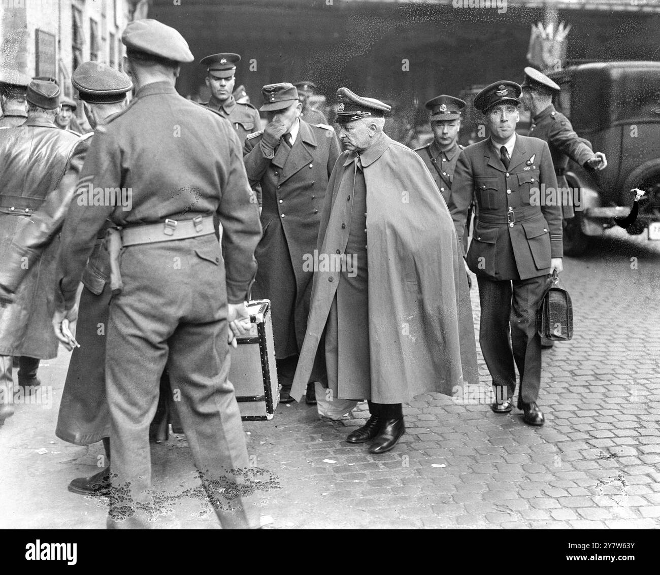 THE CLOAK OF DEFEAT Photo Shows: Wearing his field grey cloak, Lieutenant General Scheurlein, former German commander in Macedonia, stands with lieutenant General Oberausser, holding his nose, on Euston Station, departure point for a number of senior German officers passing through London.  17 May 1945 Stock Photo