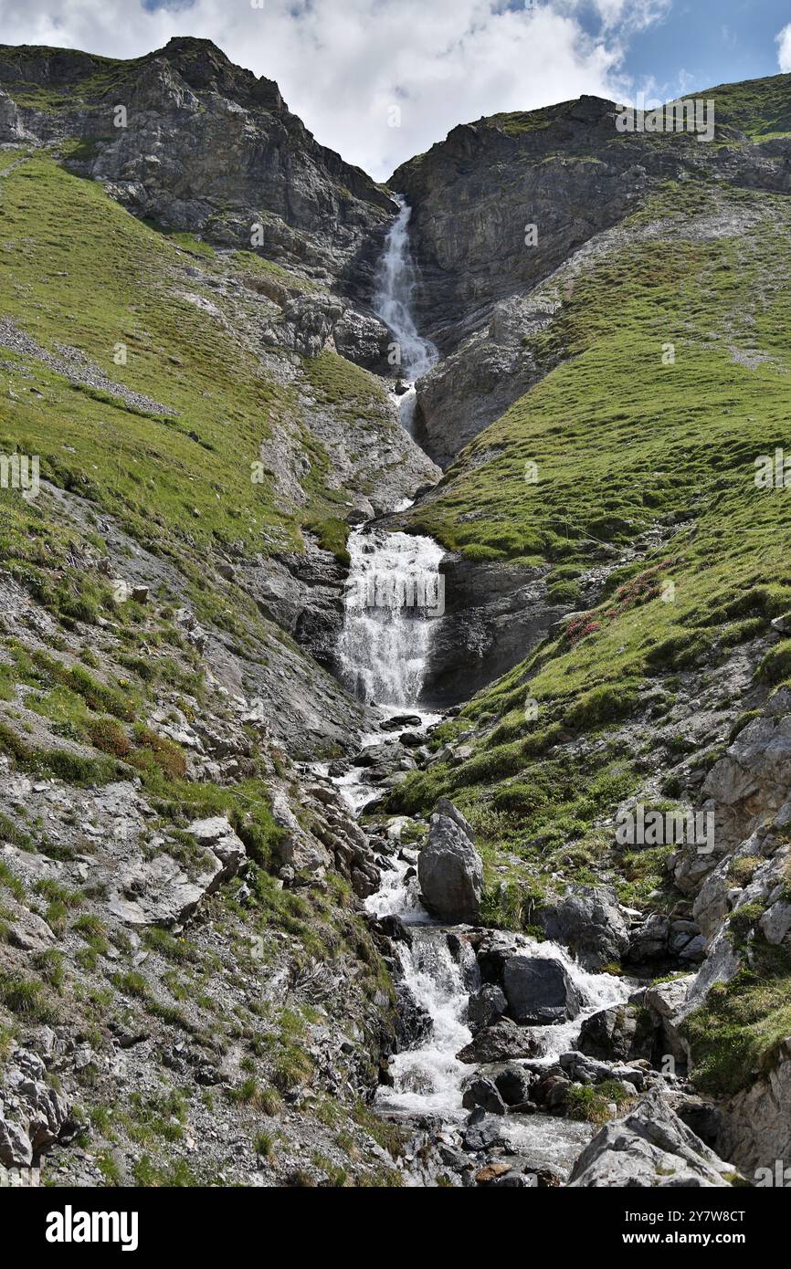 Majestic waterfall cascades down the rocky slopes of Braulio Valley in Lombardy, Italy, under a bright blue sky kissed by clouds Stock Photo