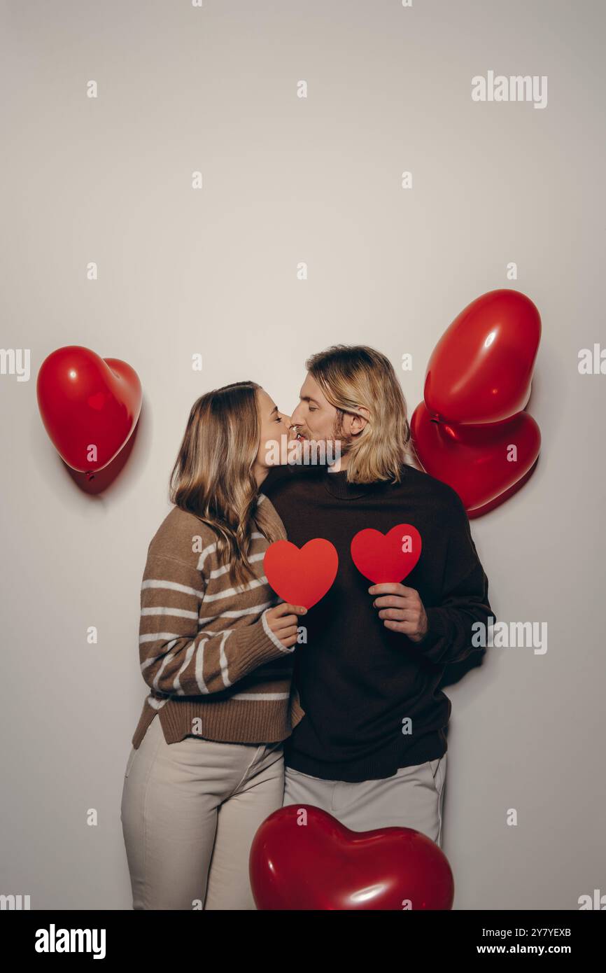 Loving couple holding heart shape Valentines cards and kissing on beige ...