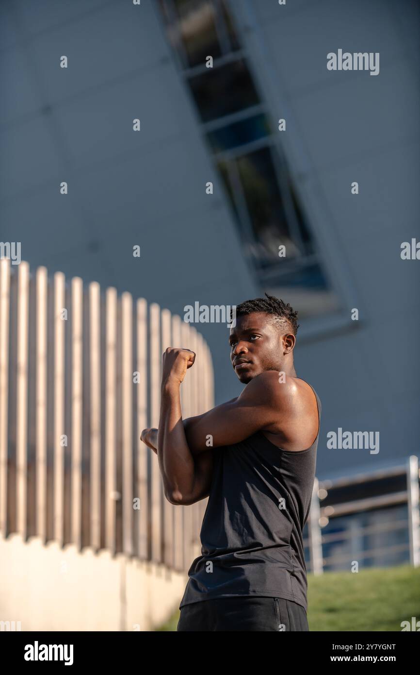 Concentrated young African man in sportswear doing stretching exercises while training outdoors Stock Photo