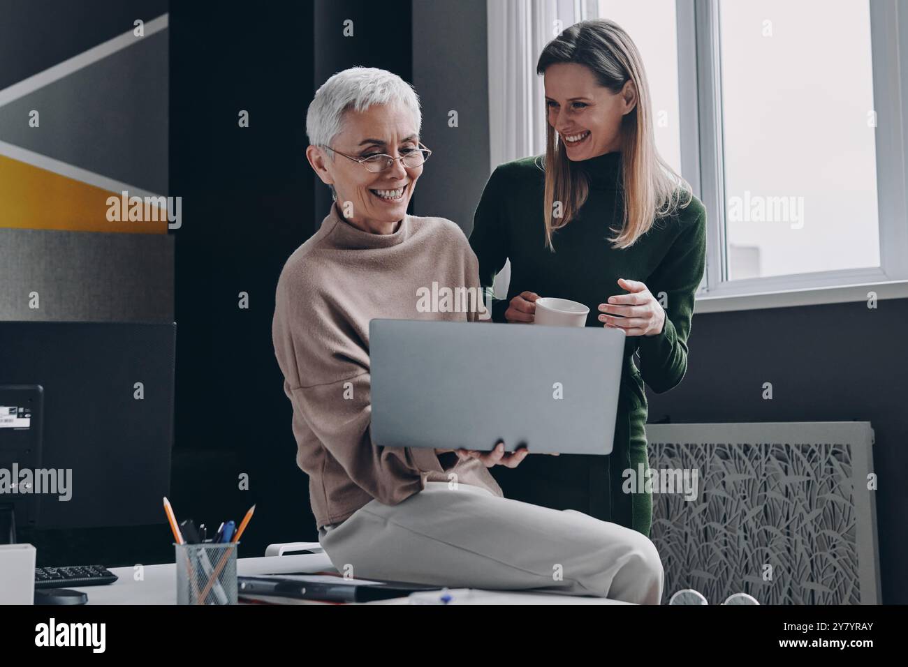 Two happy women using laptop and communicating while working in office ...