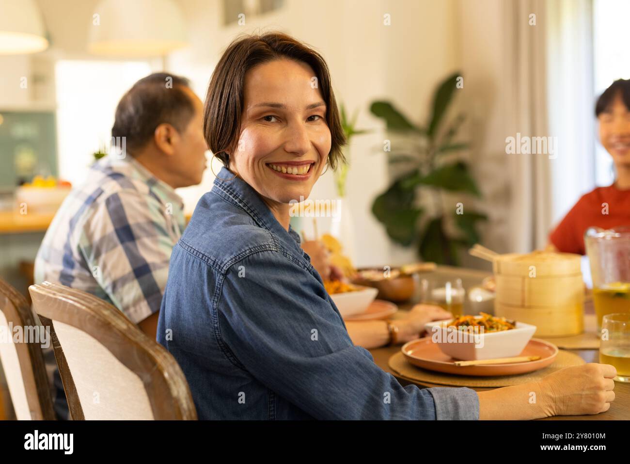 At home, Smiling middle-aged woman enjoying meal with family at dining table, sharing happy moments Stock Photo