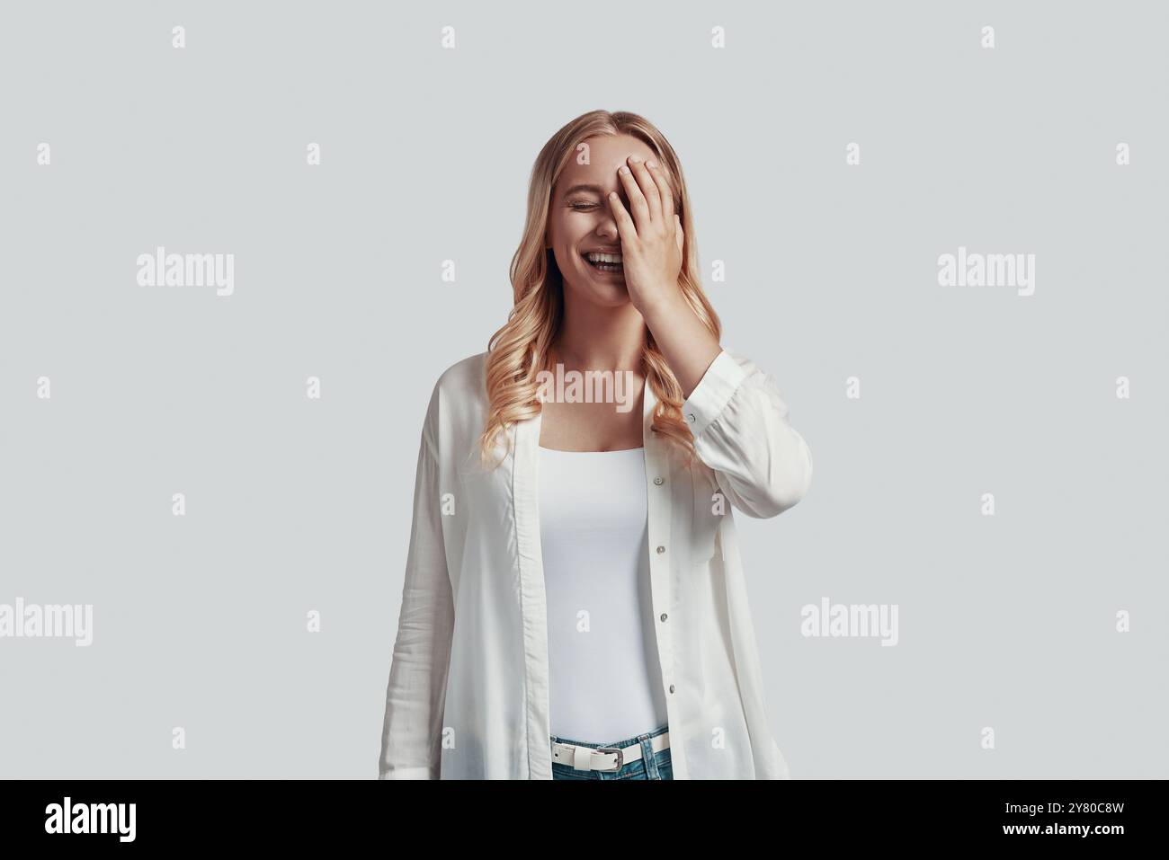 Beautiful young woman covering face with hand and smiling while ...