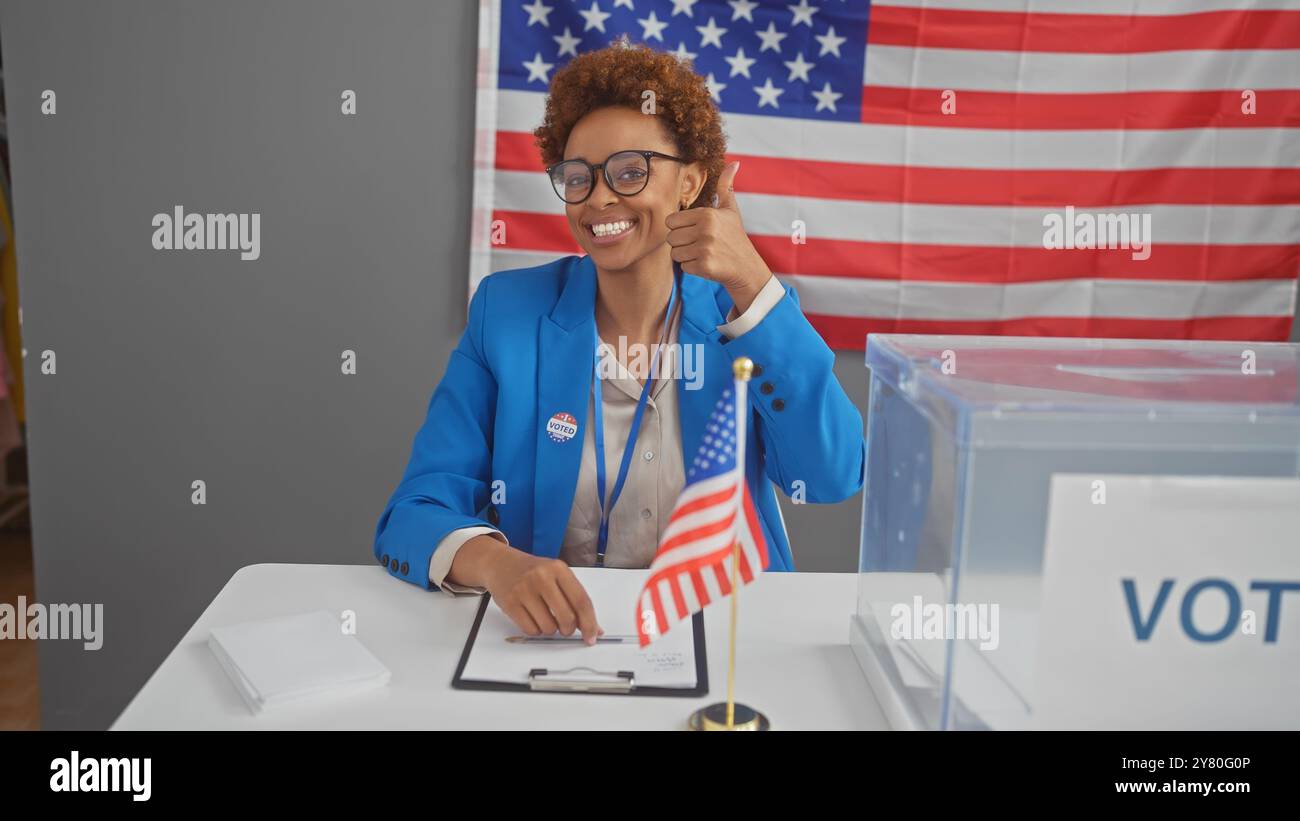 Smiling african american woman giving thumbs-up in polling station with ...