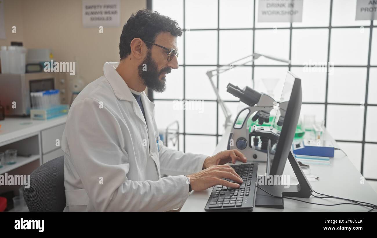 Mature bearded man in lab coat working at computer in modern laboratory ...