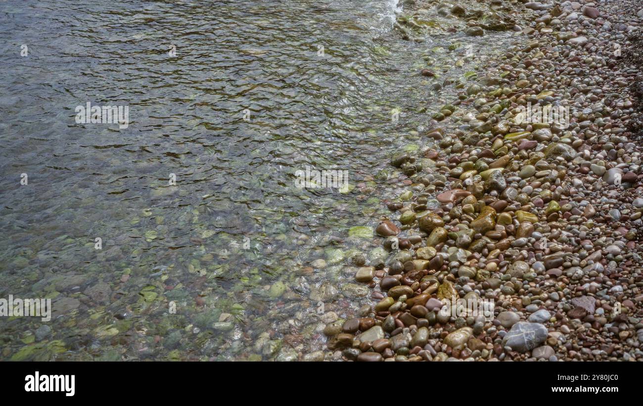 Clear water gently laps over colorful pebbles on a serene beach ...