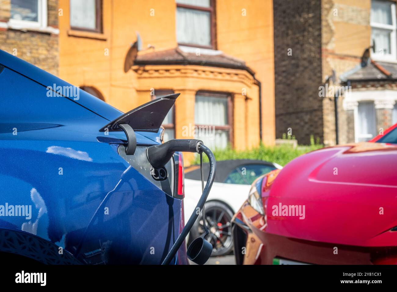 An electric car plugged in on charge on a residential street in central ...