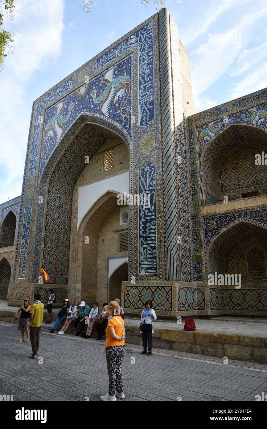 Bukhara, Uzbekistan - Sept 12, 2024: Tourist near  tilted central portal of Nadir Divan Beghi Madrasah decorated with mythical birds of happiness, Lya Stock Photo