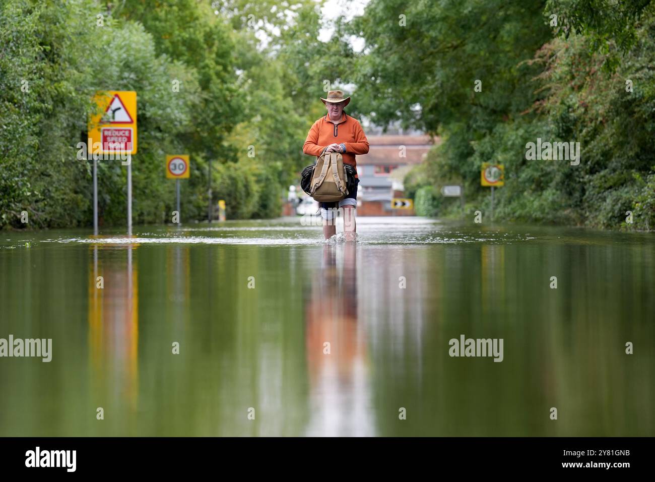 A man makes his way along a flooded road in Offord Cluny, Cambridgeshire. Further showery spells are expected across England, but drier, more settled weather conditions are set to arrive in the coming days. Picture date: Wednesday October 2, 2024. Stock Photo