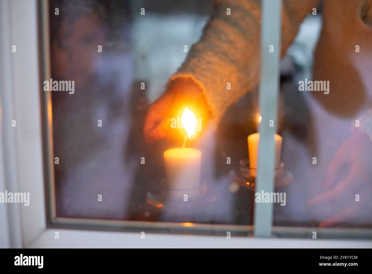 A person inside a house lights a candle seen through a frosty window on a cold day. Stock Photo