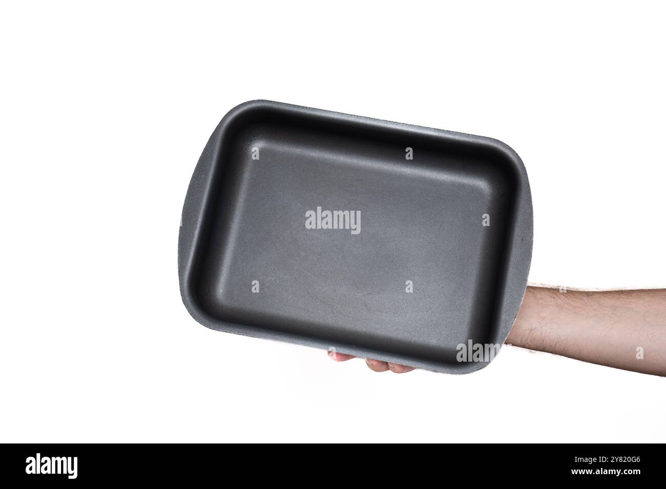 Empty, black, rectangular deep baking tray or casserole. Held by hand by Caucasian male hand. Close up studio shot, isolated on white. Stock Photo