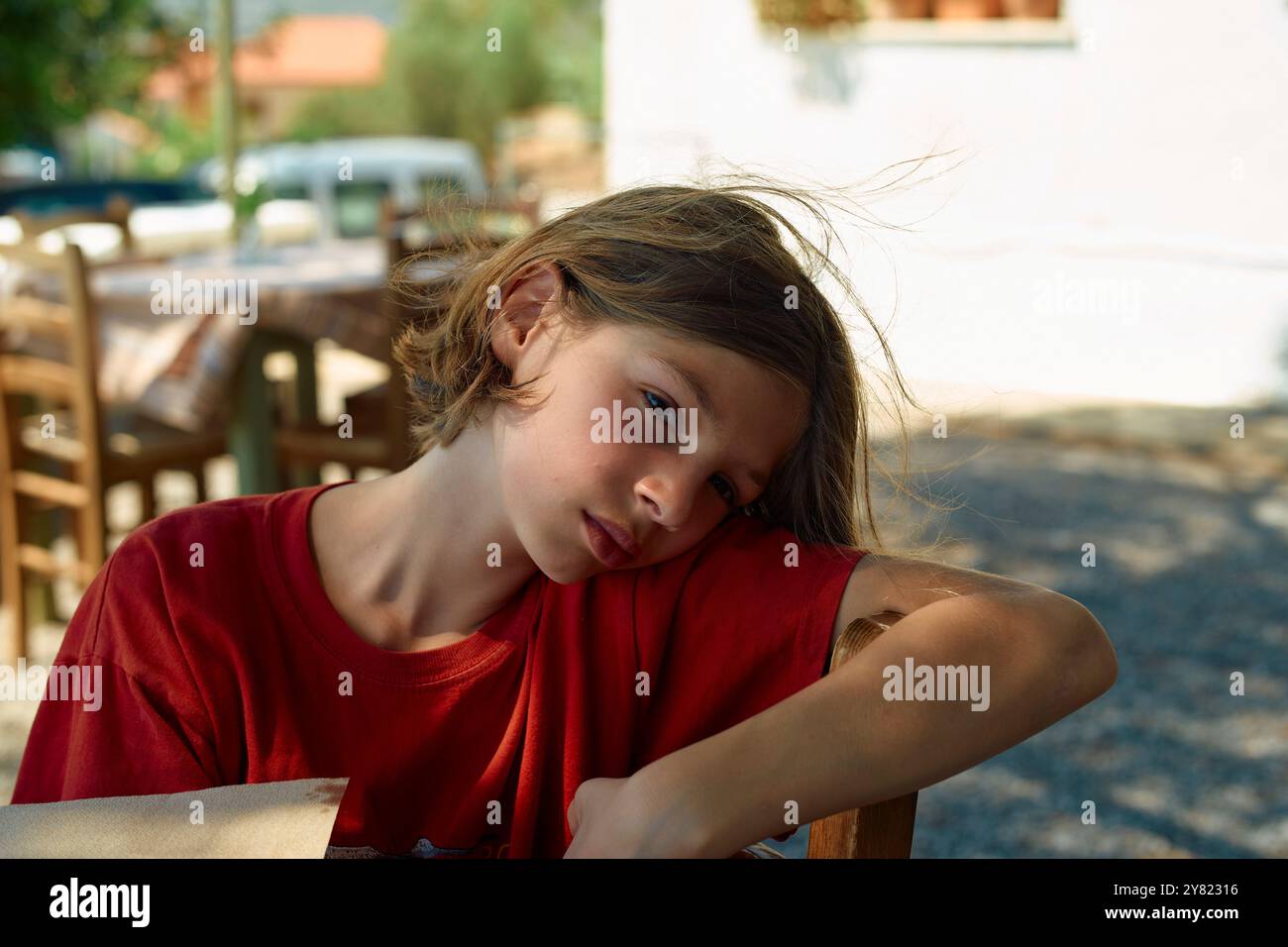 Young boy resting his head on his arm at a wooden table outdoors. Stock Photo