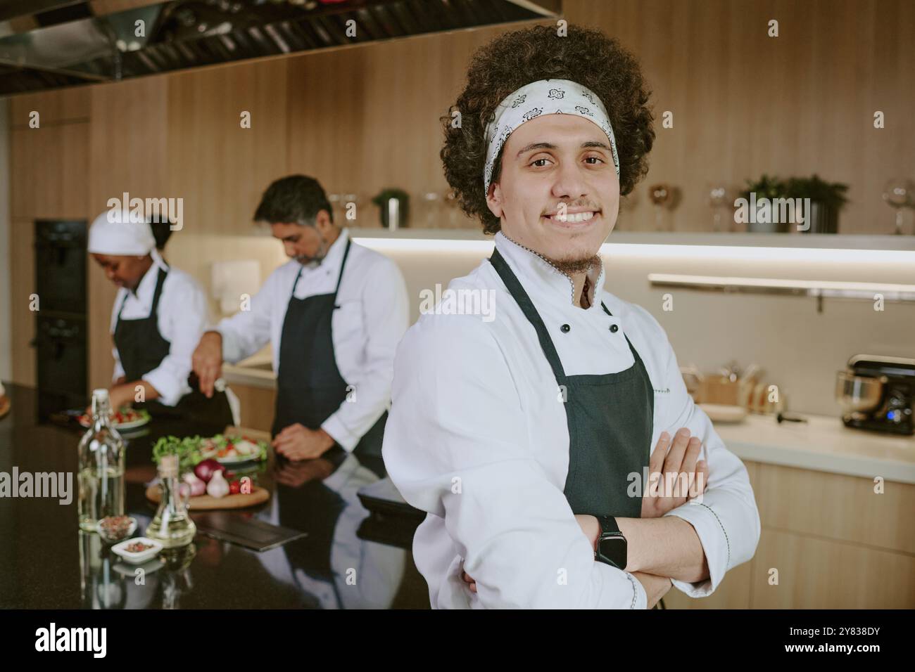 Medium close up portrait of young curly haired sous chef smiling widely while posing for photo Stock Photo