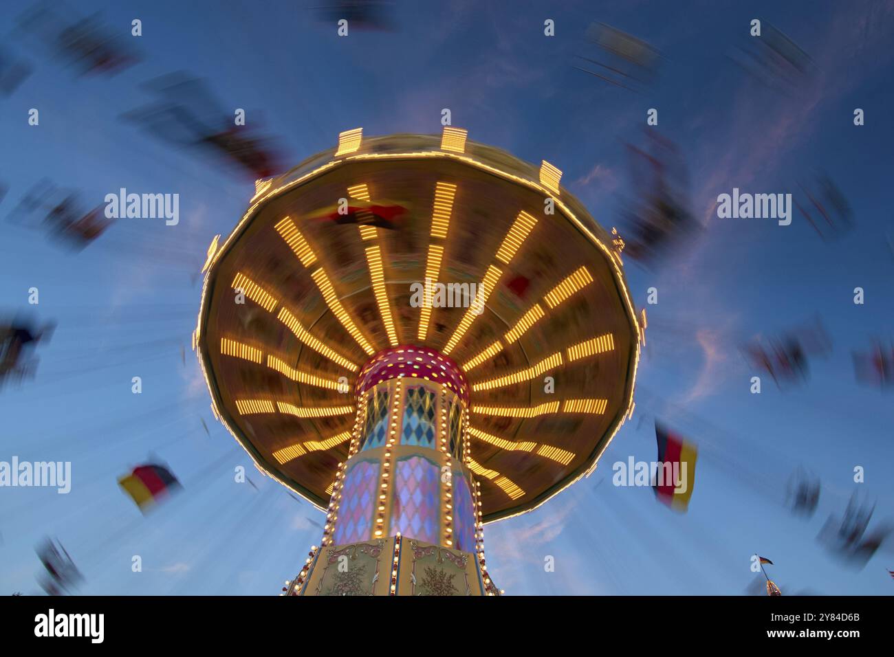 An illuminated carousel at dusk, spinning fast, in front of a blue sky ...