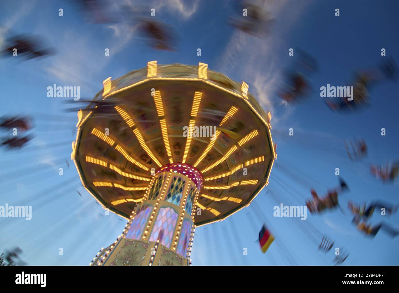 An illuminated carousel at dusk, spinning fast, in front of a blue sky ...