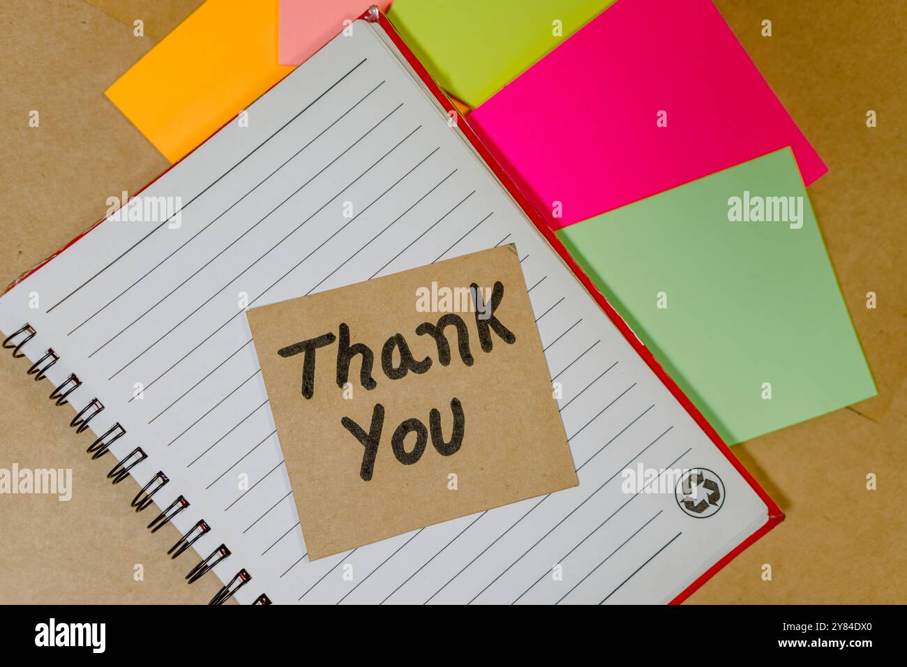 Thank you phrase written on recycled cardboard with a background of a lined notebook and post-it notes Stock Photo