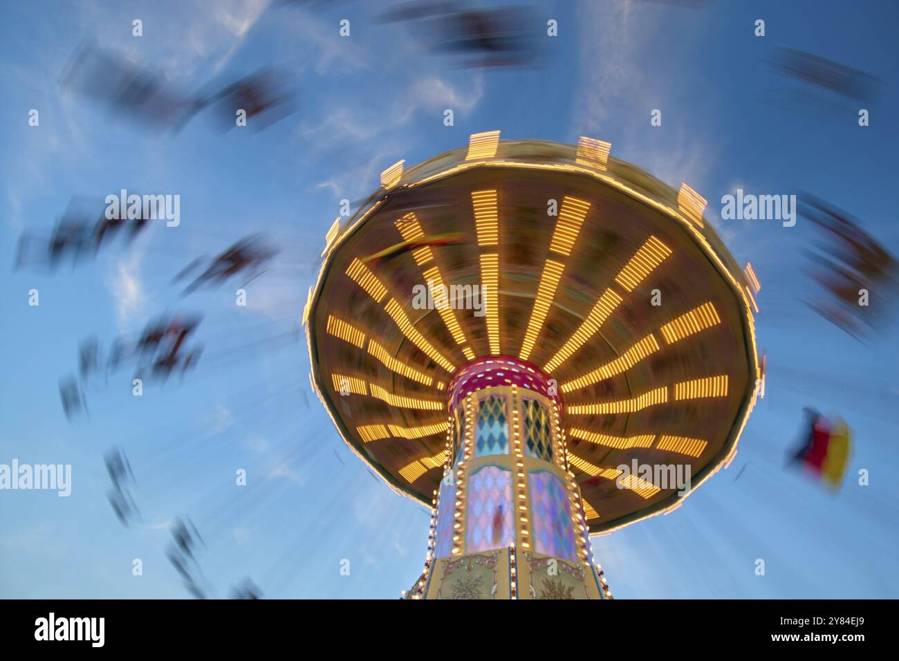 An illuminated carousel at dusk, spinning fast, in front of a blue sky ...