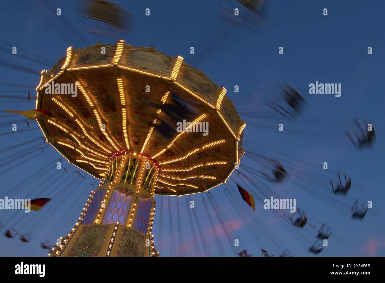 An illuminated carousel at dusk, spinning fast, in front of a blue sky ...