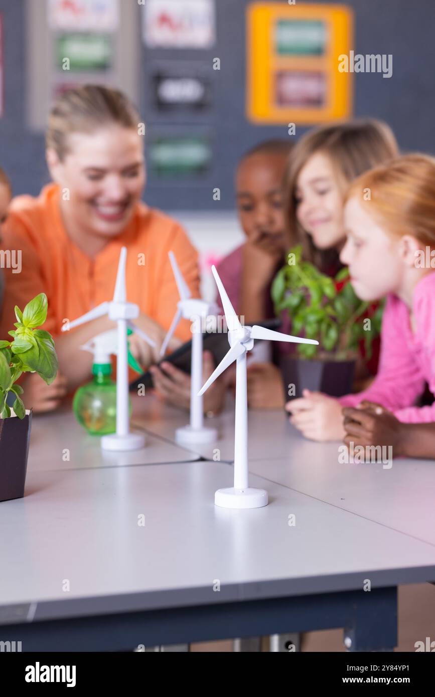 In school, female teacher and diverse students examining wind turbine models and plants together Stock Photo