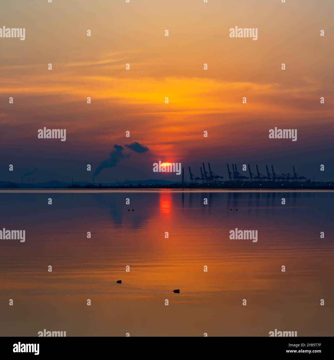 A serene sunset over calm waters in Oido, with warm colors reflecting on the still surface as the sun dips below the horizon. Stock Photo