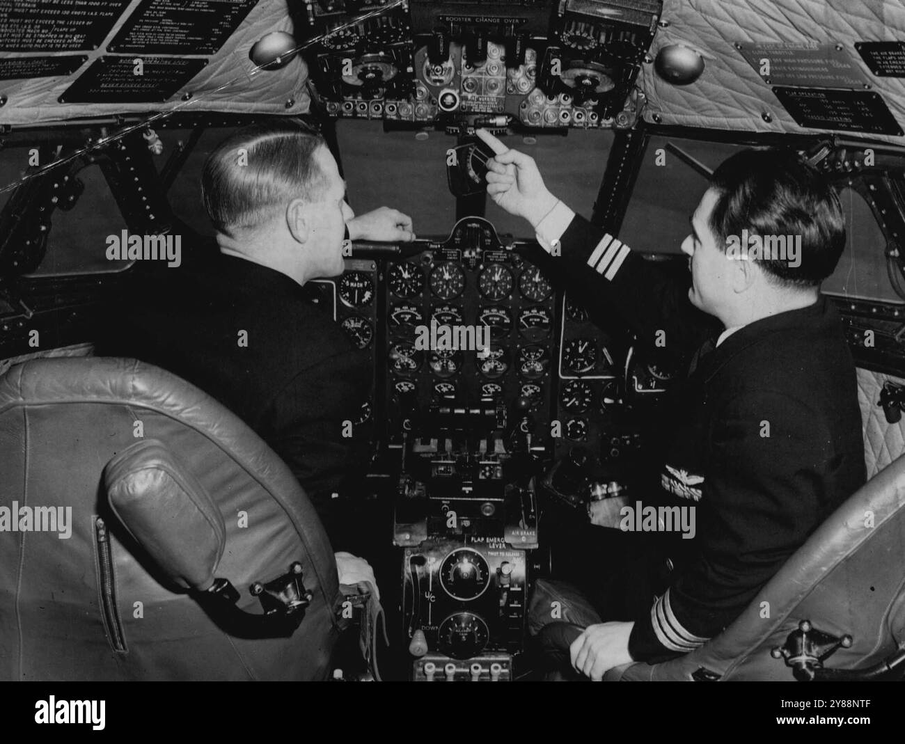 Men Who Will Fly The Comets Learn Their Secrets -- Instructor Captain Ernest Rodley (right) of Esher, Surrey, explaining controls to Captain Trevor Marsden of Bournemouth, one of the trainees, in a Comet cockpit at London Airport.Pilots and other British Overseas Airways air crewmen are getting ready at the B.O.A.C. Training Centre, London Airport, to fly Britain's new Comet jet airliners when they go into service. They are undergoing a 4-month conversion course preparing them for the change-over from piaton-engined aircraft to jet planes. The course includes study at the De Havilland factory, Stock Photo