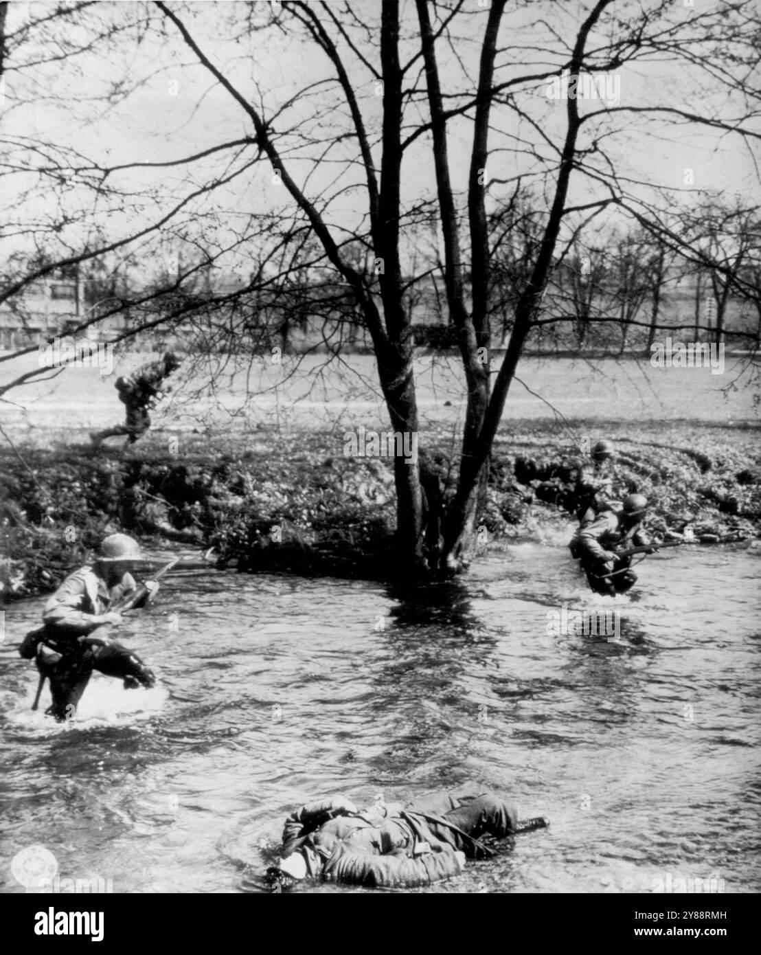 Yanks Stream past Dead SS Trooper -- Cut down by a Machine Gun burst, a Dead German SS trooper lies in the Schleuse river near Waldau, Germany, as Yanks of the 26th division splash by to ford the steam and attack enemy positions in nearby pine Forests. April 18, 1945. (Photo by AP Wirephoto). Stock Photo