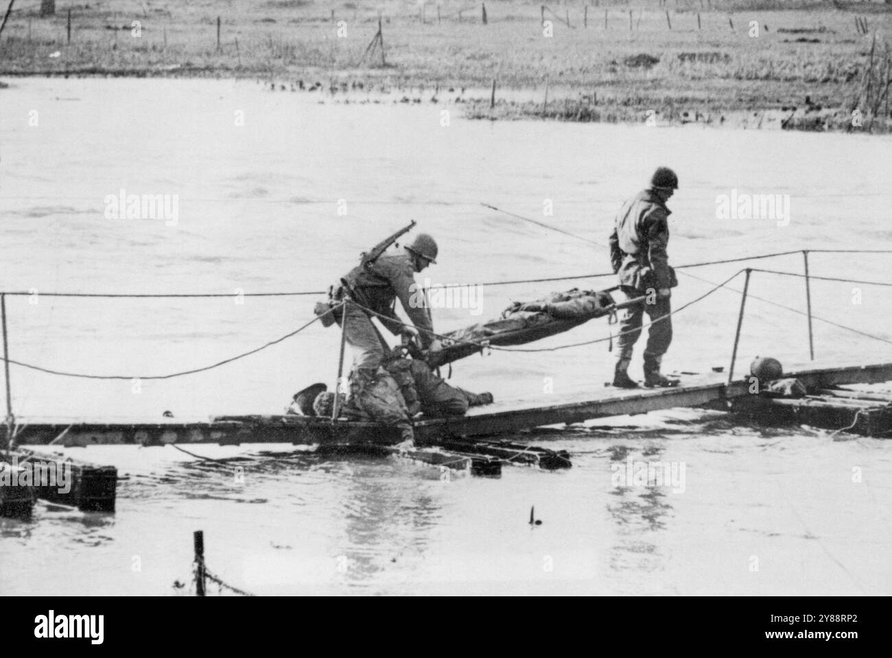 Wounded Yank carried across Roer -- Stretcher bearers carry a wounded American soldier over the body of a dead buddy as negotiate a temporary Bridge over the Roer River in Germany. The soldier was wounded and his buddy killed during crossing of German Barrier  by the yank forces,follow which  the Americans swept to the Rhine River. March 2, 1945. (Photo by Associated Press Photo). Stock Photo