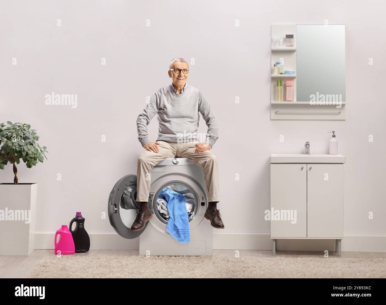 Happy elderly man sitting on a washing machine in a bathroom Stock Photo