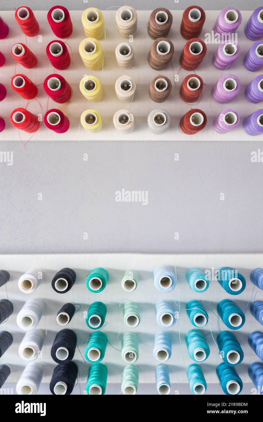 Multi-colored threads in spools and bobbins for sewing in a sewing workshop on a vertical Stock Photo