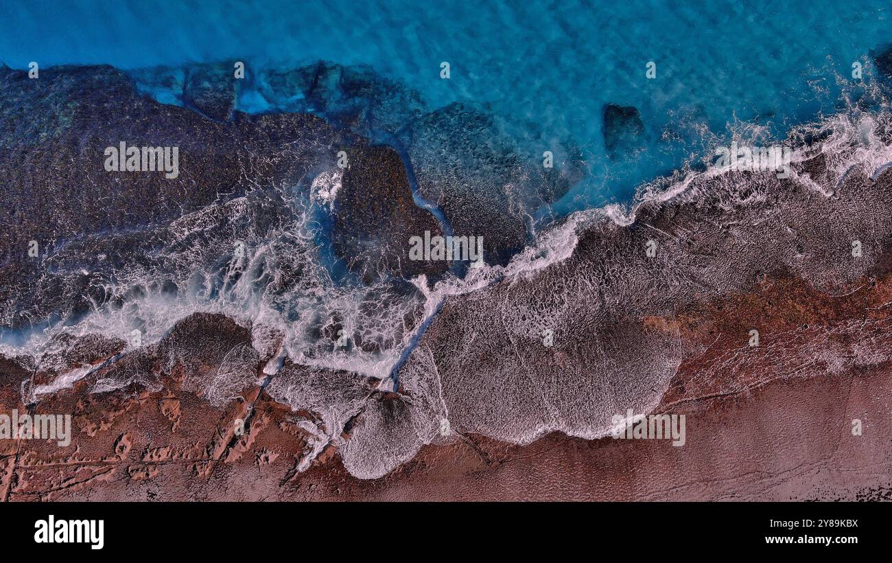 waves crashing over a red rocky reef Stock Photo
